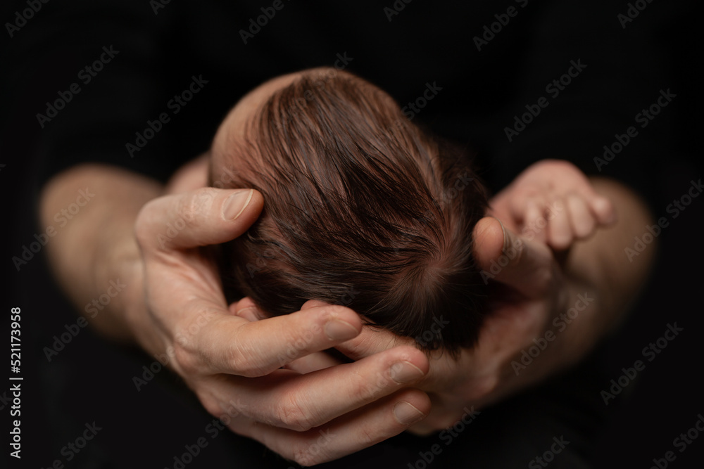 Adorable beautiful newborn baby cradled in its mothers hands looking up with a look of wonderment Adorable beautiful newborn baby cradled in its mothers hands looking up with a look of wonderment