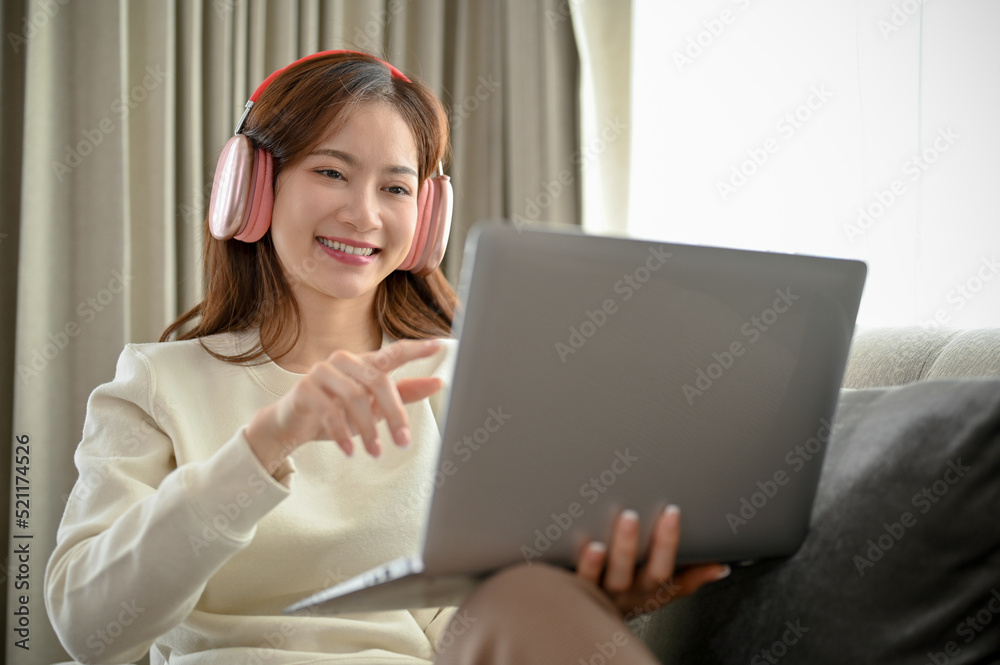 Happy young Asian woman wearing headphones and watching movie on laptop computer. Happy young Asian woman wearing headphones and watching movie on laptop computer.