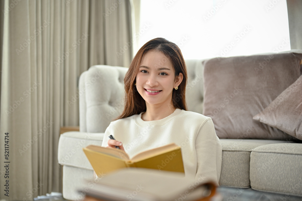 Gorgeous Asian woman sits in modern minimal living room holding a book or novel. Gorgeous Asian woman sits in modern minimal living room holding a book or novel.