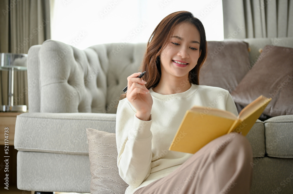 Attractive young Asian woman sits in the minimal living room enjoying reading a book. Attractive young Asian woman sits in the minimal living room enjoying reading a book.
