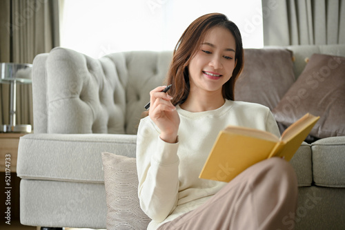 Attractive young Asian woman sits in the minimal living room enjoying reading a book.