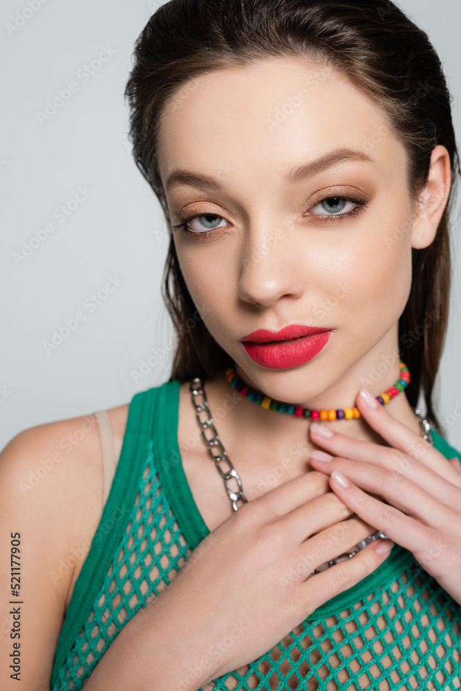 young and stylish woman with red lips touching beads necklace while posing isolated on grey