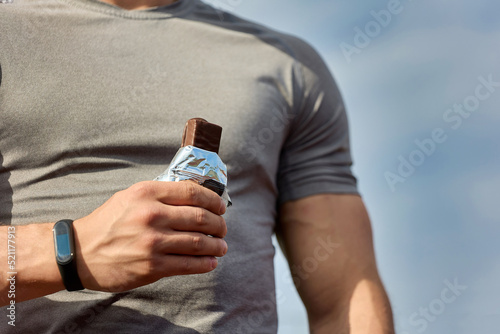 Muscular athlete rests after a workout, an athlete eats a protein bar. A young athlete eats an energy bar while enjoying chocolate after a hard workout at the stadium