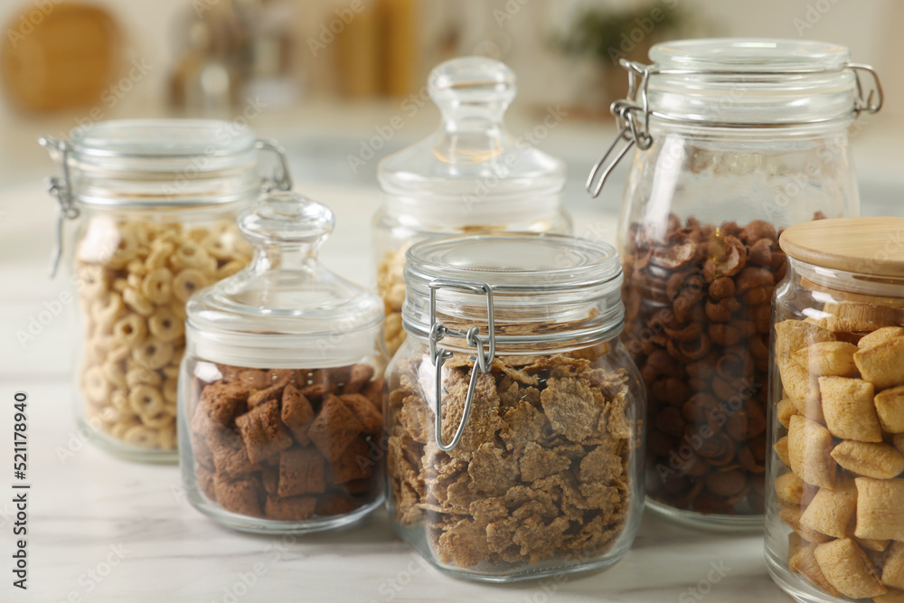 Glass containers with different breakfast cereals on white marble table indoors Glass containers with different breakfast cereals on white marble table indoors