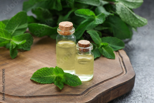 Bottles of essential oil and mint on grey table, closeup