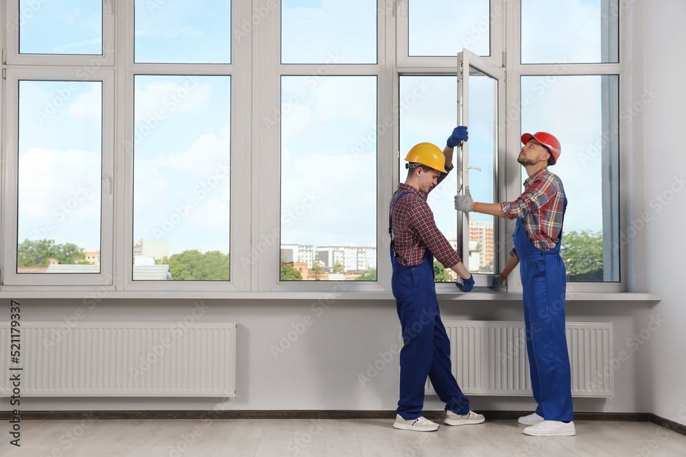Workers in uniform installing plastic window indoors Workers in uniform installing plastic window indoors