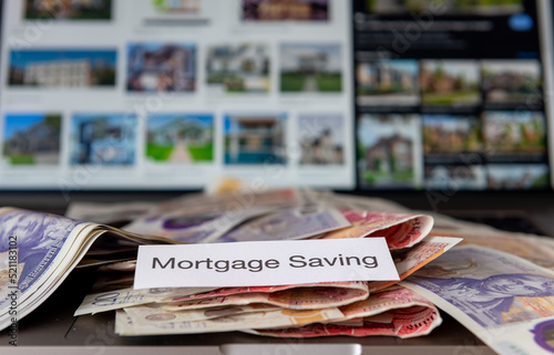 A mortgage saving concept with bank notes and blurred images of properties on a computer in the background.