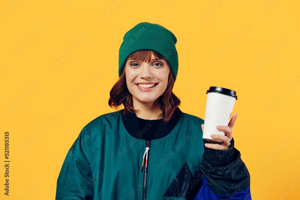 a happy, joyful woman stands on a yellow background in a stylish jacket and holding a coffee glass in her hands, smiling pleasantly while looking at the camera a happy, joyful woman stands on a yellow background in a stylish jacket and holding a coffee glass in her hands, smiling pleasantly while looking at the camera