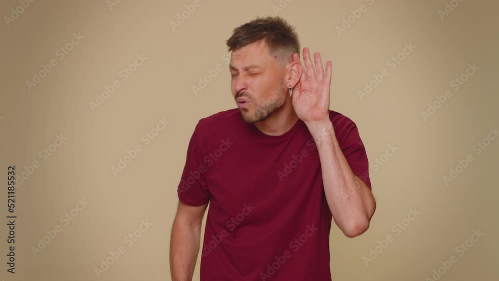 I cant hear you. What. Young man trying hear you, looking confused and frowning, keeping arm near ear for louder voice, asking to repeat, to hear information, deafness. One guy on beige background I cant hear you. What. Young man trying hear you, looking confused and frowning, keeping arm near ear for louder voice, asking to repeat, to hear information, deafness. One guy on beige background