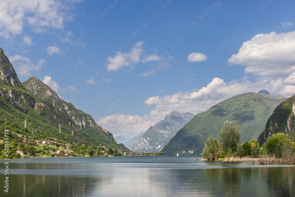 Panoramic shot of calm waters of alpine lake Idro (Lago d'Idro) surrounded by rocks and wooded mountains. Brescia, Lombardy, Italy