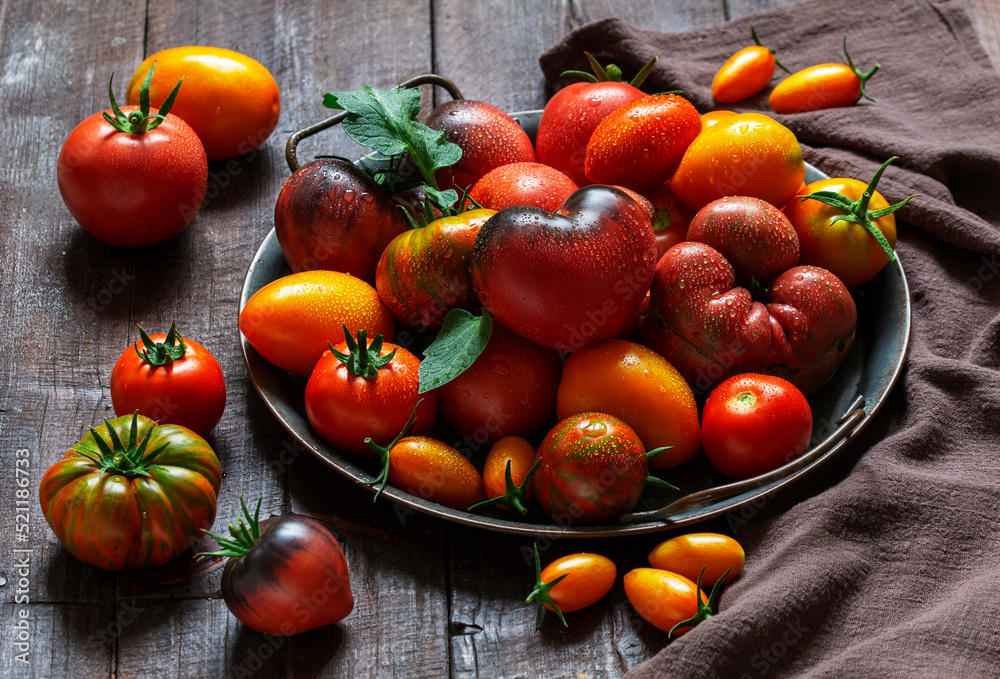 Tomatoes of various varieties and sizes on an iron tray on a wooden table.