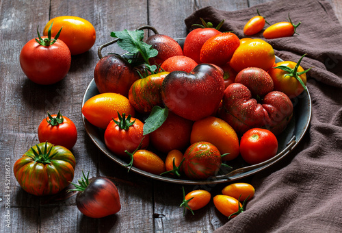 Tomatoes of various varieties and sizes on an iron tray on a wooden table.
