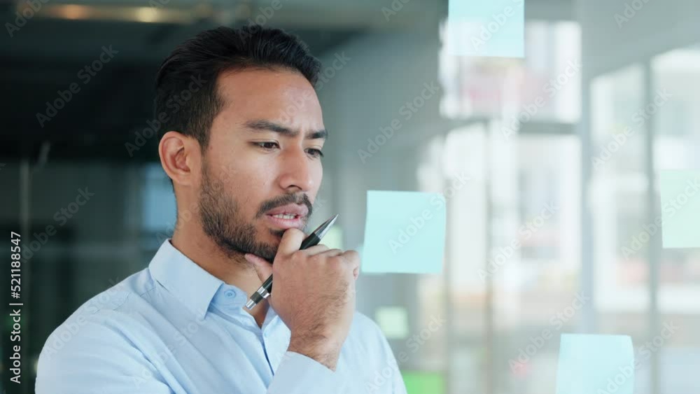Professional man brainstorming and planning, thinking of marketing ideas while writing on sticky notes at work. Focused male making a visual board while researching a strategy and managing his tasks