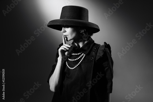 Portrait of beautiful woman in image of famous fashion designer posing in stylish black hat. Black and white photography. Secrets of fashion