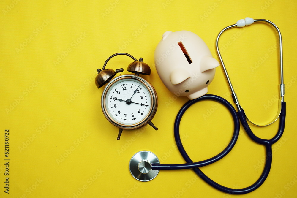 Alarm clock with piggy saving and stethoscope top view on yellow background Alarm clock with piggy saving and stethoscope top view on yellow background