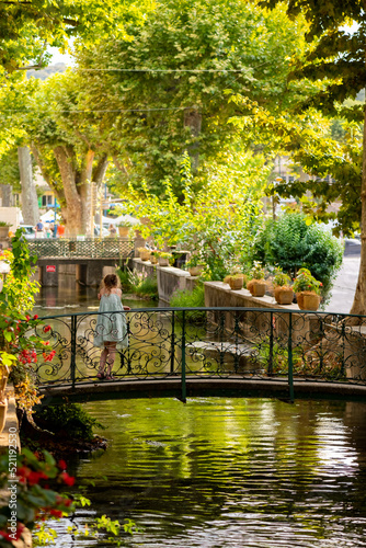 Gourdargues village in the Cèze valley in provence, southern France. Idyllic alley way called “Venise Gardoise“ with big plane trees and water canal flowing underneath a pedestrian bridge with girl.