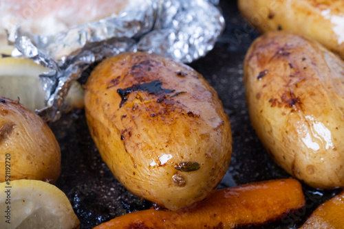 Close-up of appetizing oven baked potatoes and carrots with baked salmon in foil in the background.