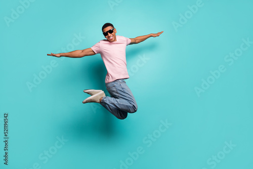 Full length photo of pretty childish guy wear pink t-shirt jumping high arms sides empty space isolated teal color background