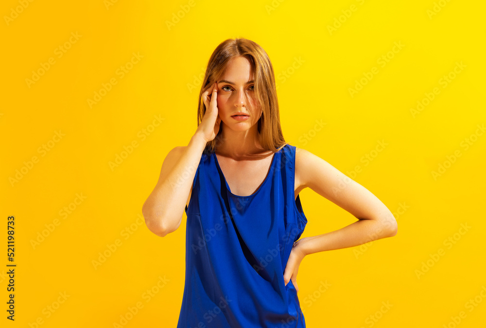 Young sad girl, student touching her head with hand isolated on bright yellow background. Concept of health, medicine, emotions and facial expressions Young sad girl, student touching her head with hand isolated on bright yellow background. Concept of health, medicine, emotions and facial expressions