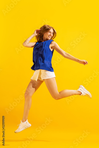 Happy young girl, student jumping isolated on bright yellow background. Concept of beauty, art, fashion, emotions and facial expressions