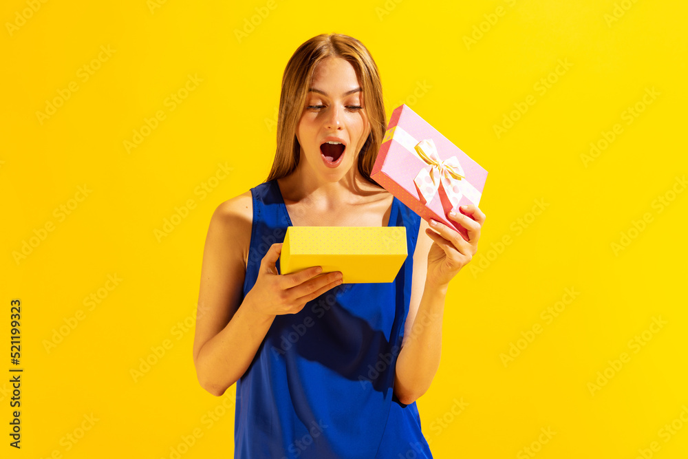 Thrilled young beautiful blond girl holding gift box isolated on yellow background. Concept of emotions, holidays, inspiration, sales, ad. Thrilled young beautiful blond girl holding gift box isolated on yellow background. Concept of emotions, holidays, inspiration, sales, ad.