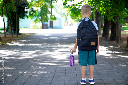 Back to school.Portrait of an elementary school student.First grader.The beginning of classes. a boy with a backpack holds a bottle of drinking water in his hands, a view of the back