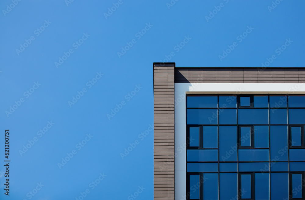 Fototapeta premium The edge of the facade of a modern building with glass mirrored windows against the blue sky. Place for text