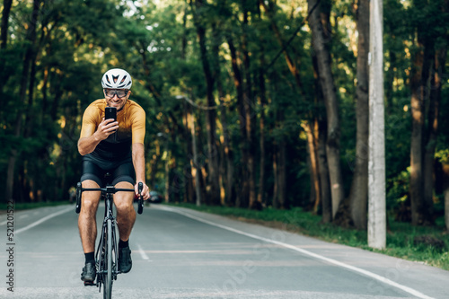 Athletic man in sport clothes riding a bike in the nature and using a smartphone