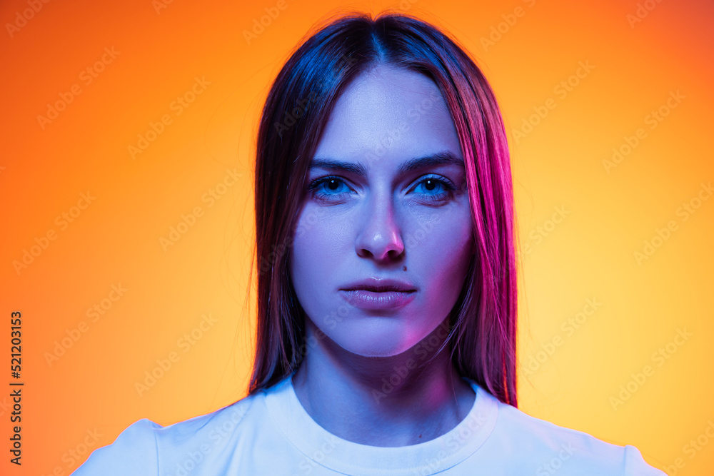 Closeup face of young attractive girl looking at camera isolated on orange color background in neon light. Concept of emotions, facial expressions Closeup face of young attractive girl looking at camera isolated on orange color background in neon light. Concept of emotions, facial expressions