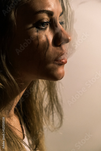 Crying young woman releasing cigarette smoke from mouth. Portrait of a side view of an unhappy woman experiencing an emotional crisis in life. Domestic psychological and physical violence. Vertical