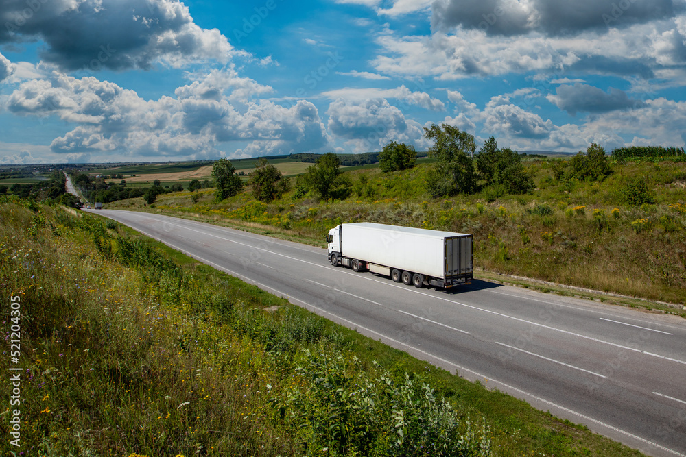 white cargo truck on the highway. asphalt road among green fields and beautiful clouds. cargo delivery and transportation concept