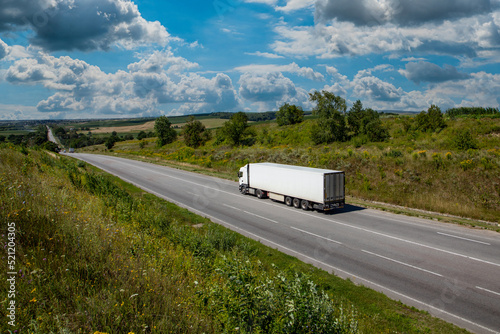 white cargo truck on the highway. asphalt road among green fields and beautiful clouds. cargo delivery and transportation concept