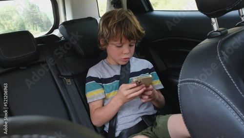 Little cute caucasian boy using mobile phone in the car with durk interior salon. photo