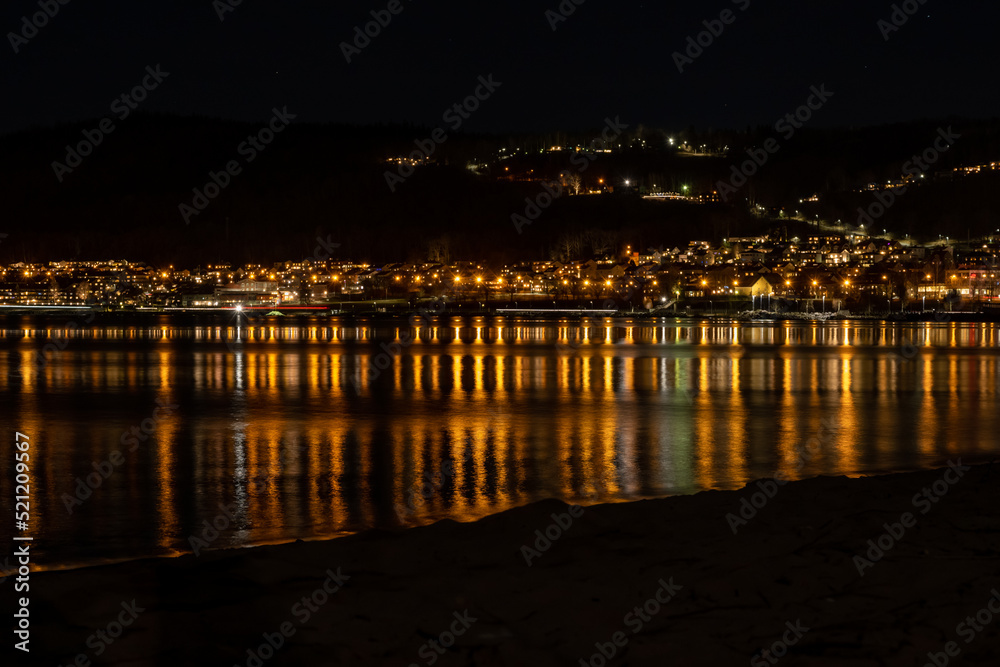 Lights from a hillside town reflect in a lake at night