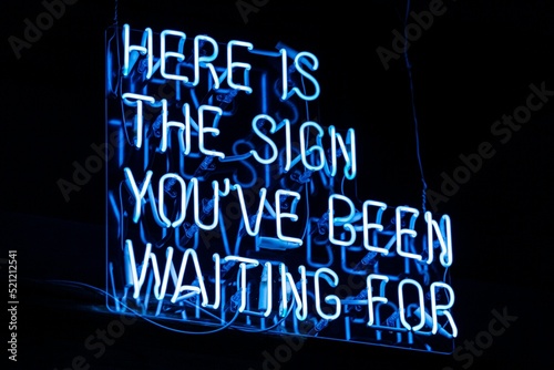 Illuminated blue motivation "here is the sign you've been waiting for" sign on a black background