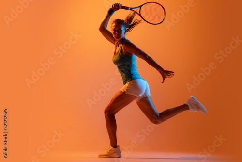 Portrait of woman, professional tennis player training isolated over orange studio background in neon light. Strength © Lustre