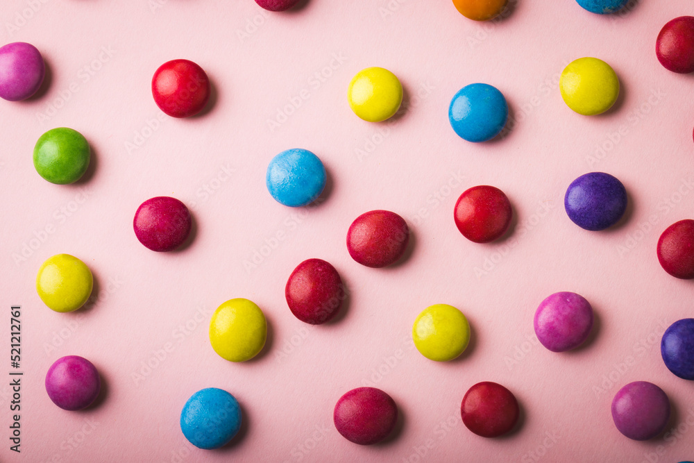 Directly above view of multi colored chocolate candies scattered over pink background Directly above view of multi colored chocolate candies scattered over pink background