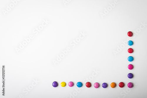Overhead view of multi colored chocolate candies arranged by copy space over white background