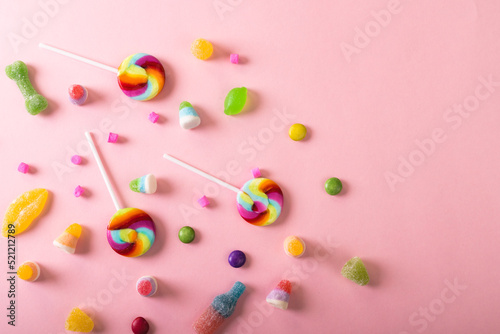 Directly above view of lollipops with chocolate and sugar candies scattered against pink background