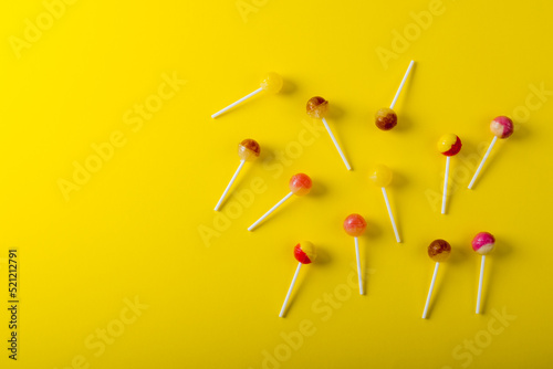 Overhead view of lollipops scattered by copy space against yellow background photo