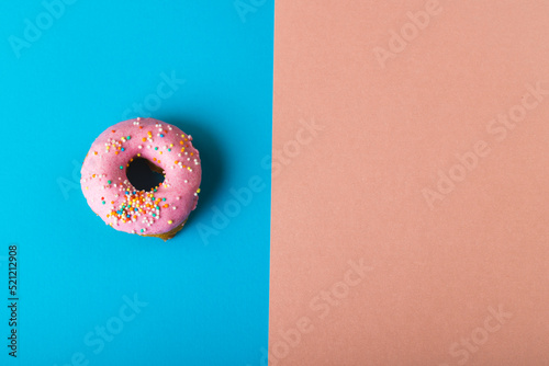 Overhead view of fresh pink donut with sprinklers by copy space on two tone colored background