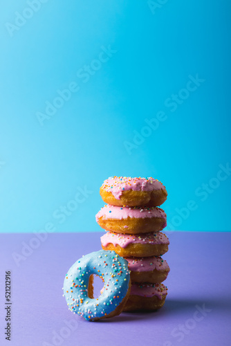 Fresh donuts with sprinklers stacked against blue background with copy space