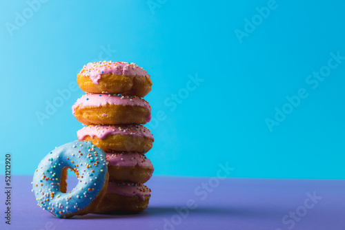 Fresh donuts with sprinklers stacked against copy space over pink background