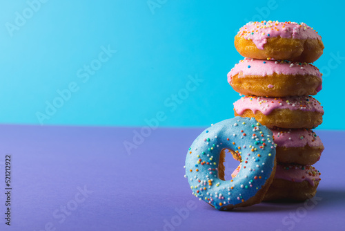 Close-up of fresh donuts with sprinklers stacked against two tone colored background with copy space