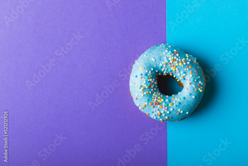 Overhead view of fresh donut with sprinklers by copy space against two tone colored background
