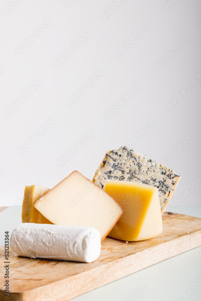 Various cheese on wooden board against white background with copy space