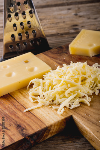 Close-up of grated cheese on wooden board by grater at table, copy space