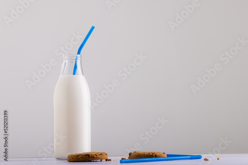 Milk bottle with straw by cookies against white background, copy space