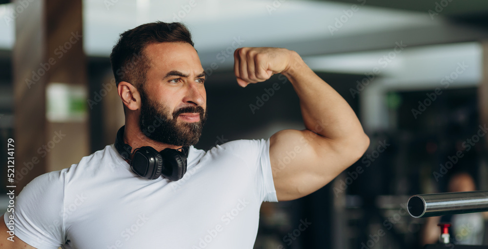 smiling sports man in white t-shirt showing his muscles in the gym
