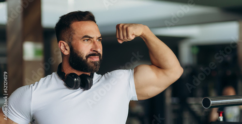 smiling sports man in white t-shirt showing his muscles in the gym